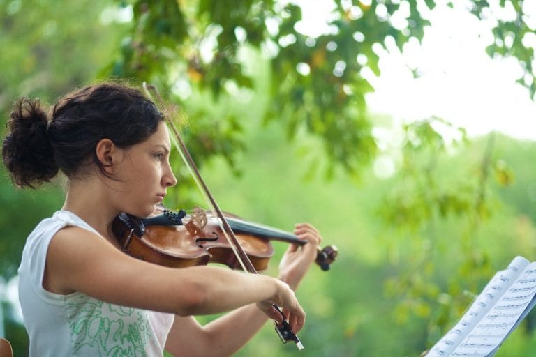 Teenager playing viola with trees in the background